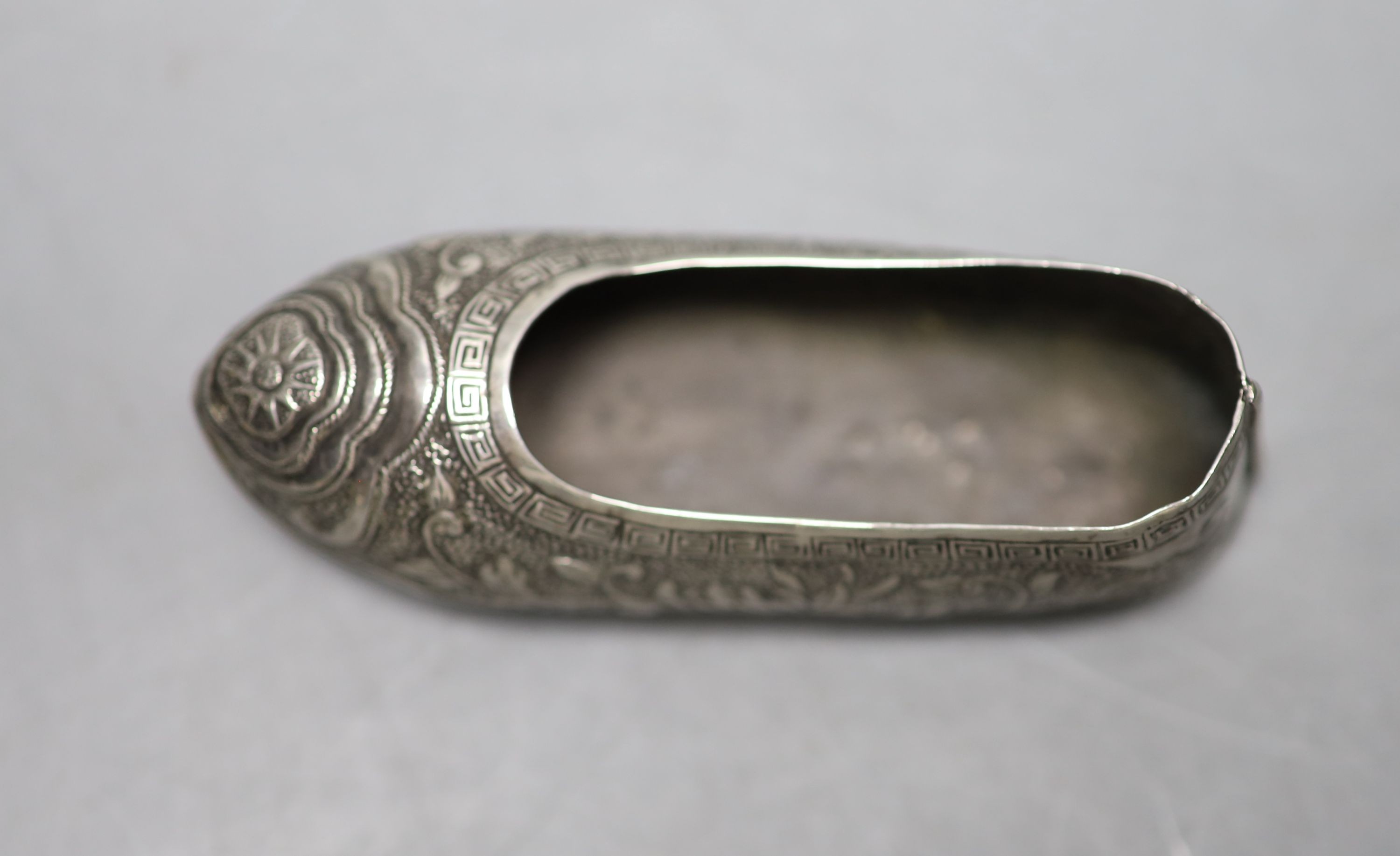 An early 20th century Chinese engraved white metal pin cushion, modelled a s a shoe, (lacking cushion), maker HC, 85mm.